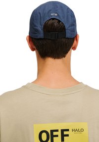 Granatowa czapka z dziurkowanymi bokami, regulowany pasek z tyłu. Beżowy T-shirt z dużą żółtą grafiką z napisem "OFF HALO."