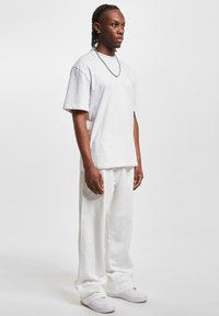 Hvid bomulds-t-shirt og matchende løstsiddende bukser med et afslappet design. Outfittet inkluderer hvide sneakers og en sølvfarvet kædehalskæde.