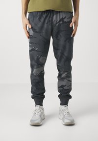 Kamouflagebyxor i mörkgrå nyanser med dragsko, ribbade muddar och sidofickor, kombinerat med ljusgrå sportskor.