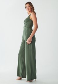 Groene jumpsuit met een aansluitende bovenkant, zijcut-out en brede broekspijpen. Glad materiaal met een geplooid detail in de taille en dunne bandjes.