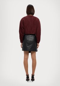Maglione corto testurizzato color bordeaux con maniche lunghe abbinato a una mini gonna in pelle nera. Sandali neri con tacco alto completano l'outfit.