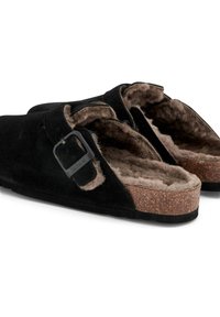 Svarta mocka tofflor med faux fur-foder, justerbart spänne och korksål. Platt design med öppen häl för enkel på- och avtagning.