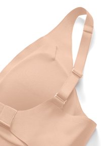 Reggiseno senza cuciture color carne con spalline regolabili e coppe sagomate, progettato per un supporto fluido e comfort.