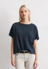 Dunkelblaues Baumwoll-T-Shirt mit kurzen Ärmeln, weitem Ausschnitt, lockerer Passform und glatter Textur, kombiniert mit hellen Hosen.