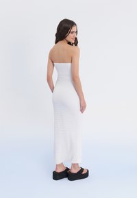 Weißes strapless Maxikleid aus strukturiertem Stoff mit figurbetontem Schnitt, kombiniert mit schwarzen Plattformsandalen.