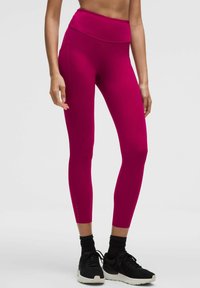 Różowe legginsy z wysokim stanem, wykonane z elastycznej tkaniny, z bocznymi szwami i małymi wycięciami przy kostkach.