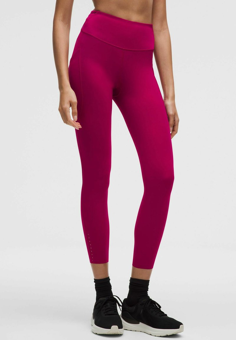 Różowe legginsy z wysokim stanem, wykonane z elastycznej tkaniny, z bocznymi szwami i małymi wycięciami przy kostkach.