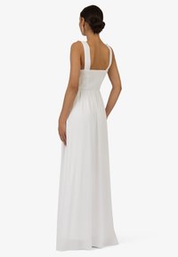 Robe maxi blanche avec larges bretelles, corsage smocké et tissu fluide. Le dos présente un décolleté carré et une texture subtile.