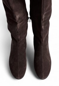 Botas marrones de ante por encima de la rodilla con una textura suave, que cuentan con cremalleras laterales y un diseño elegante y aerodinámico.