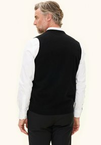 Zwarte gebreide vers met een ronde halslijn, mouwloos ontwerp en een geprofileerde stof. Gekocht over een wit overhemd met lange mouwen.
