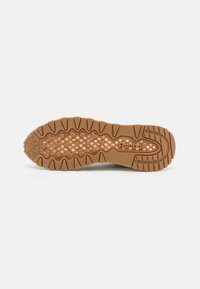 Rubber sneaker outsole in tan with textured pattern; features pronounced lugs and hexagonal depressions for traction. "Reebok" branding included.
