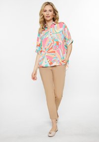 Multicolored button-up shirt featuring a geometric pattern in pink, orange, turquoise, and cream, paired with beige pants and light flats.