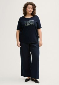 T-shirt bleu marine à manches courtes avec un imprimé "soleil". Associé à un pantalon à jambes larges à rayures et des chaussures noires à enfiler.