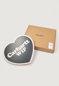 Insegna a forma di cuore Carhartt WIP nera con testo bianco, accanto a una scatola di cartone marrone etichettata "Carhartt WIP."