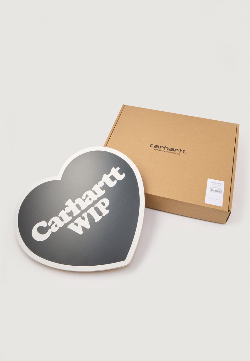Carhartt WIP hartvormig bord in het zwart met witte tekst, naast een bruine kartonnen doos met het label "Carhartt WIP."