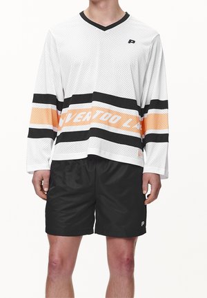 Camisa de malla blanca de manga larga con rayas horizontales negras y naranjas, combinada con pantalones cortos deportivos negros. Presenta un escote en V y detalles de logotipo.
