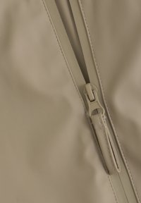 Beige stof met een gladde textuur, voorzien van een centrale rits en dikke stiksels langs de randen.