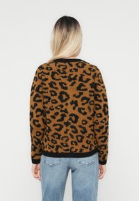 Pull en imprimé léopard marron et noir en maille, avec un col rond et des poignets côtelés. Porté avec un jean en denim léger bleu.