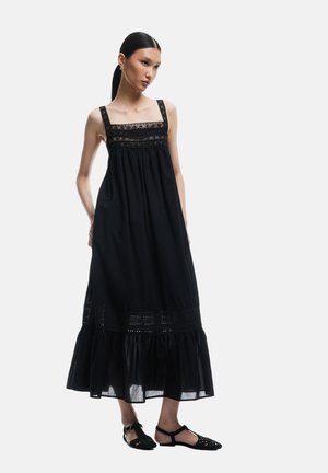 Musta maxi-mekko, jossa on säädettävät olkaimet,Texturoitu pitsikangas vartalonosa, gathered vyötärö ja kellottava helma, jossa on reikädetaljeja. Puvun kanssa mustat kengät.