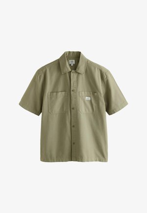 Maslinasto zelena košulja kratkih rukava s dugmadi, s dvije džepove na prsima, od kojih jedan ima malu bijelu pravokutnu oznaku.
