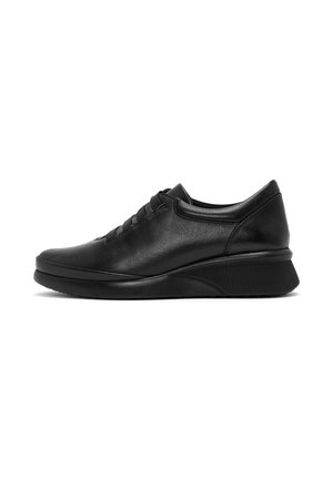 Zwarte leren sneaker met dikke gestructureerde zool, laag model en elastische veters, zijaanzicht op witte achtergrond.