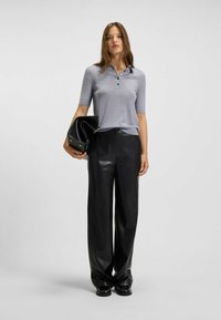 Polo grigio a maniche corte con colletto e bottoni, abbinato a pantaloni in pelle nera a vita alta e una borsa nera.