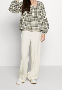 Chemisier à carreaux vert clair et noir avec des manches bouffantes, associé à un pantalon ample de couleur crème et des baskets blanches.