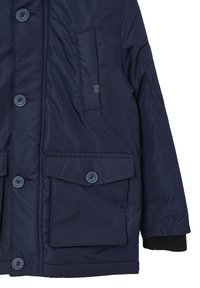 Giacca isolante blu navy con due tasche frontali, chiusure a bottone e polsini a coste. Texture liscia e dettagli di design minimalisti.