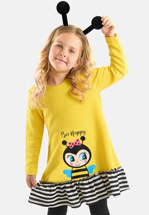 Gelbes Kleid mit langen Ärmeln, das eine Biene-Grafik und den Text "Bee Happy" zeigt. Gestreifter schwarz-weißer Volant am Saum. Schwarzes Antennen-Haarband.