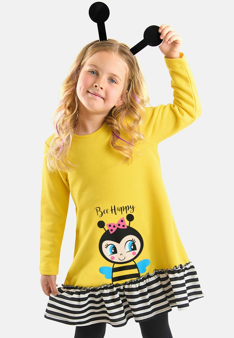 Gelbes Kleid mit langen Ärmeln, das eine Biene-Grafik und den Text "Bee Happy" zeigt. Gestreifter schwarz-weißer Volant am Saum. Schwarzes Antennen-Haarband.