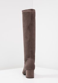 Bota alta de ante marrón hasta la rodilla con un tacón cuadrado, que presenta una textura suave y un detalle de costura mínima a lo largo del empeine.