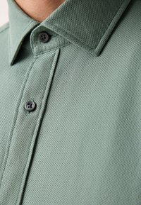 Polo verde realizzata in tessuto traspirante dalla texture, con colletto piegato e due bottoni scuri sulla patta.