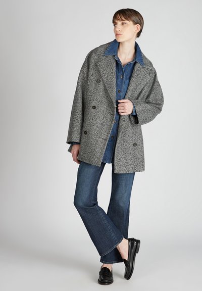 Cappotto grigio a spina di pesce con vestibilità comoda e ampi risvolti, indossato sopra una camicia di jeans blu, abbinato a jeans a campana blu e mocassini neri.