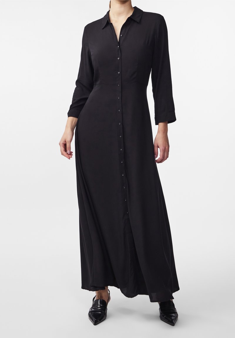 Abito maxi nero con bottoni a maniche lunghe, colletto e una texture liscia. Presenta una chiusura frontale con bottoni e fessure laterali.