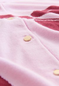 Svetloružová pletená látka s rebrovanou textúrou, zdobená detailom zlatého gombíka a farebnými akcentmi v burgundskej a bielej farbe v vzore.