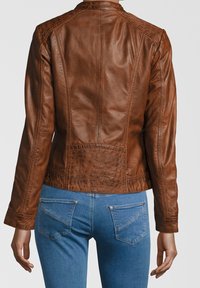 Braune Lederjacke mit taillierter Passform, ausgestattet mit strukturiertem Stich und dekorativem Rückenteil, kombiniert mit blue Denim-Jeans.