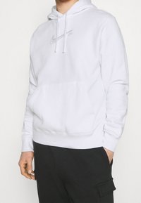 Vit Nike-hoodie med framficka, dragsko i huvan och logga broderad i silver. Mjukt tyg med ribbade muddar och fåll.