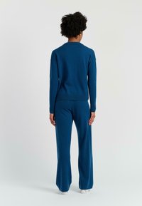 Blauwe gebreide trui met een geribde halslijn, gecombineerd met bijpassende, wijde broek. Beiden zijn gemaakt van zachte, gestructureerde stof.