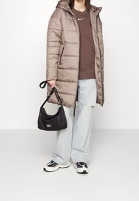 Puffer coat in light brown with a hood, paired with a dark brown sweatshirt, light blue wide-leg jeans, black shoulder bag, and sneakers.