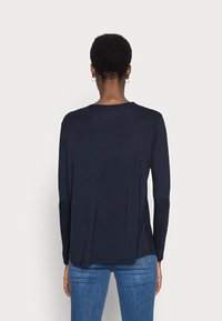 Haut à manches longues bleu marine en matériau doux, avec un col rond et des fentes latérales pour un ajustement décontracté. La vue arrière révèle une texture lisse.