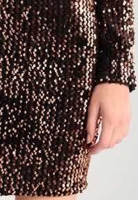 Svart paljettklänning med en figursydd design, dekorerad med roséguldpaljetter. Texturen är glansig, med en mjuk finish och långa ärmar.