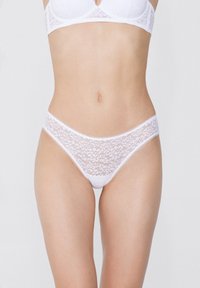String blanc en dentelle avec motifs floraux, tissu doux et ceinture élastique. Le design présente des bords festonnés et une texture semi-transparente.