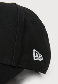 Μαύρο καπέλο από βαμβάκι με δομημένη εφαρμογή. Διαθέτει λευκό κεντημένο λογότυπο στο πλάι και υφασμάτινη υφή. Η γείσα είναι ραμμένη στη ραφή.