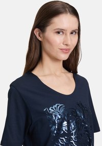 Mørkeblå bomulds T-shirt med korte ærmer og rund halsudskæring. Har et skinnende blomstermotiv på forsiden.