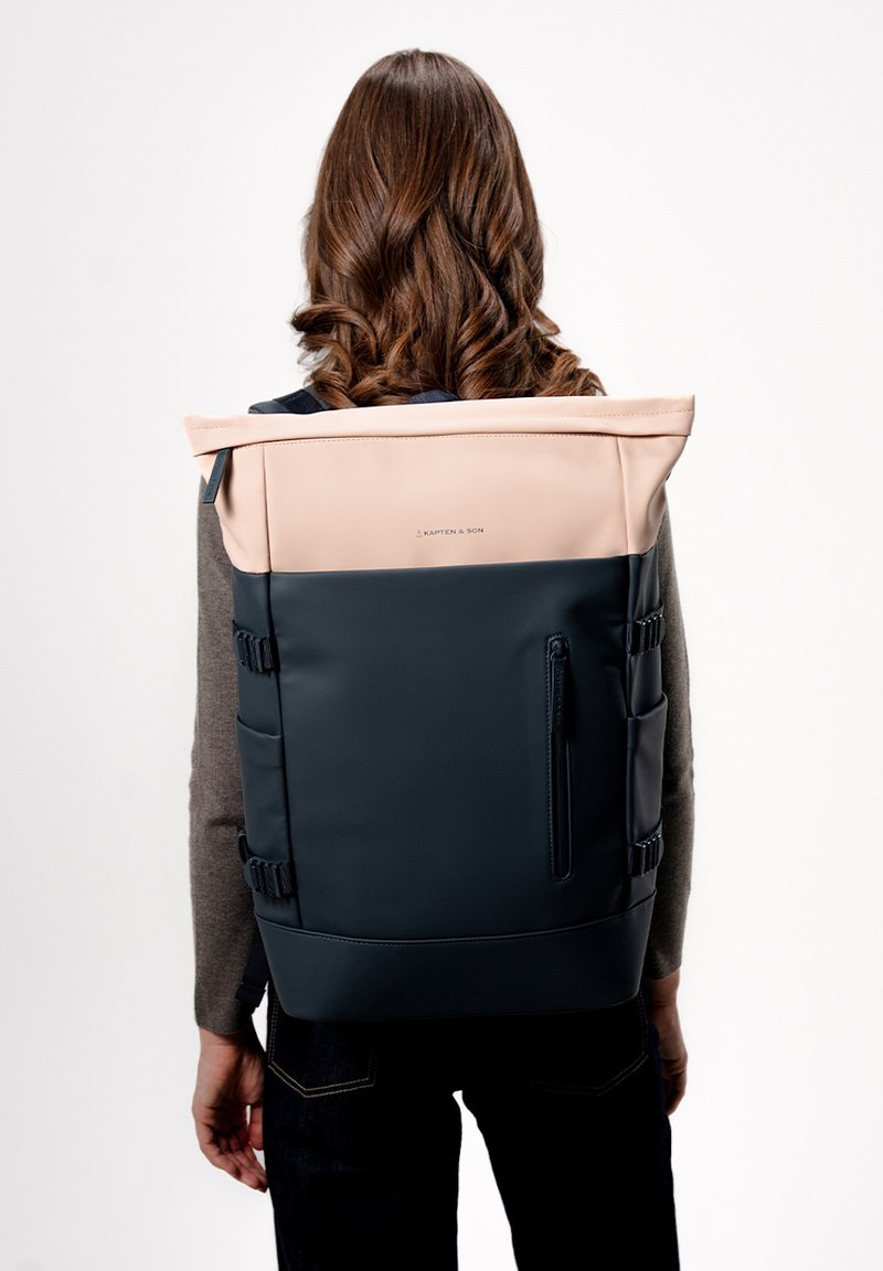 Černý a světle růžový voděodolný batoh s nastavitelnými popruhy, designem s rolovacím víkem, zipovou kapsou a bočními úložnými oddíly.