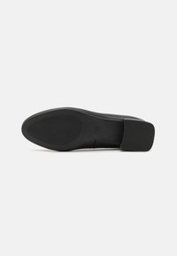 Semelle de chaussure noire avec un extérieur lisse et texturé. Bout rond et petit talon carré. Imprimer discret du logo près de la zone du talon.