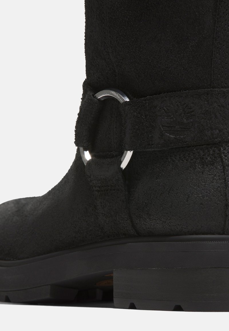 Stivale alla caviglia in suede nero con finitura testurizzata, dettaglio ad anello in argento e suola nera robusta. Presenta un branding sottile sulla fascia.