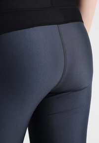 Leggings de tiro alto, elásticos y de color azul oscuro con una textura suave. Presentan una cinturilla negra y costuras visibles.