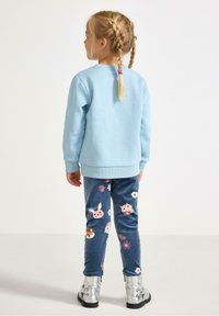Felpa azzurra chiara abbinata a leggings in pile blu navy con motivi di animali e fiori. Stivaletti argentati alla caviglia completano l'outfit.