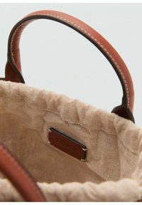 Canvas tote bag with brown leather handles. Interior features a gathered top and a small, brown label with embossed text.